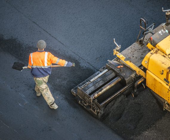 Workers lay a new asphalt coating using hot bitumen. Work of heavy machinery and paver. The view from the top